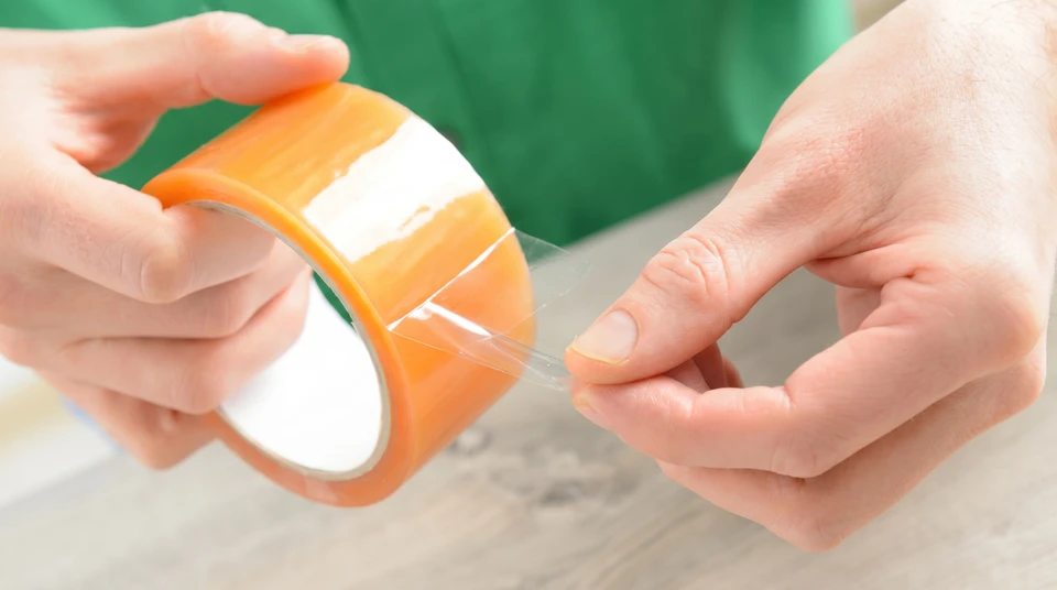Mains avec rouleau d'emballage transparent, ruban adhésif